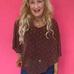 Woman wearing a sheer brown polka dot mesh poncho with a wide boat neck layered over a tank and trousers