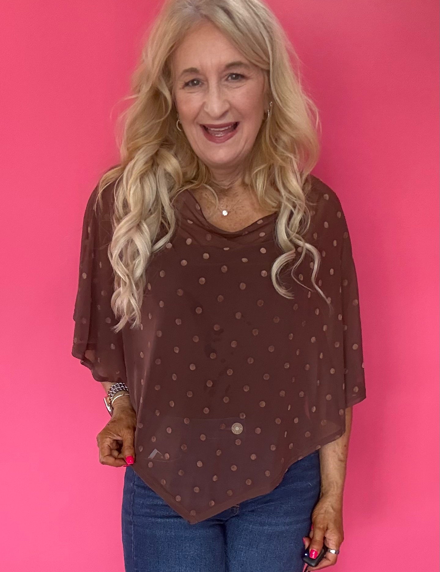 Woman wearing a sheer brown polka dot mesh poncho with a wide boat neck layered over a tank and trousers