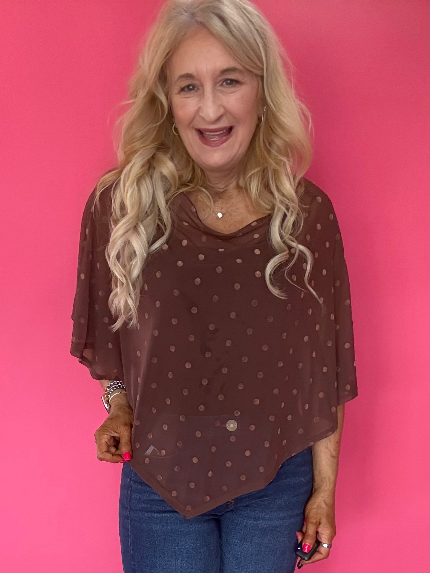 Woman wearing a sheer brown polka dot mesh poncho with a wide boat neck layered over a tank and trousers