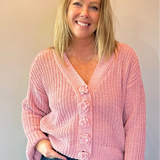 Woman wearing a pink cardigan and blue jeans standing against a plain wall.