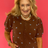 Woman wearing a cocoa brown polka dot cardigan styled open over a simple top with denim