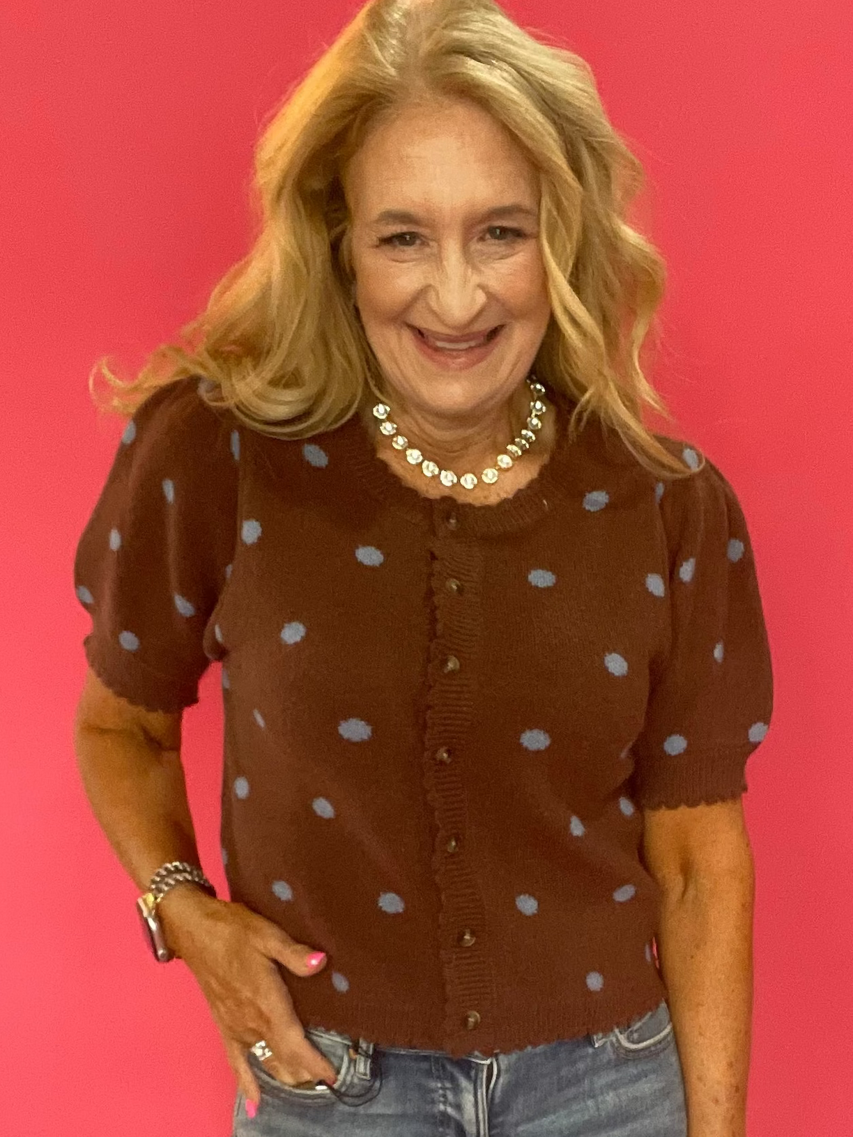 Woman wearing a cocoa brown polka dot cardigan styled open over a simple top with denim
