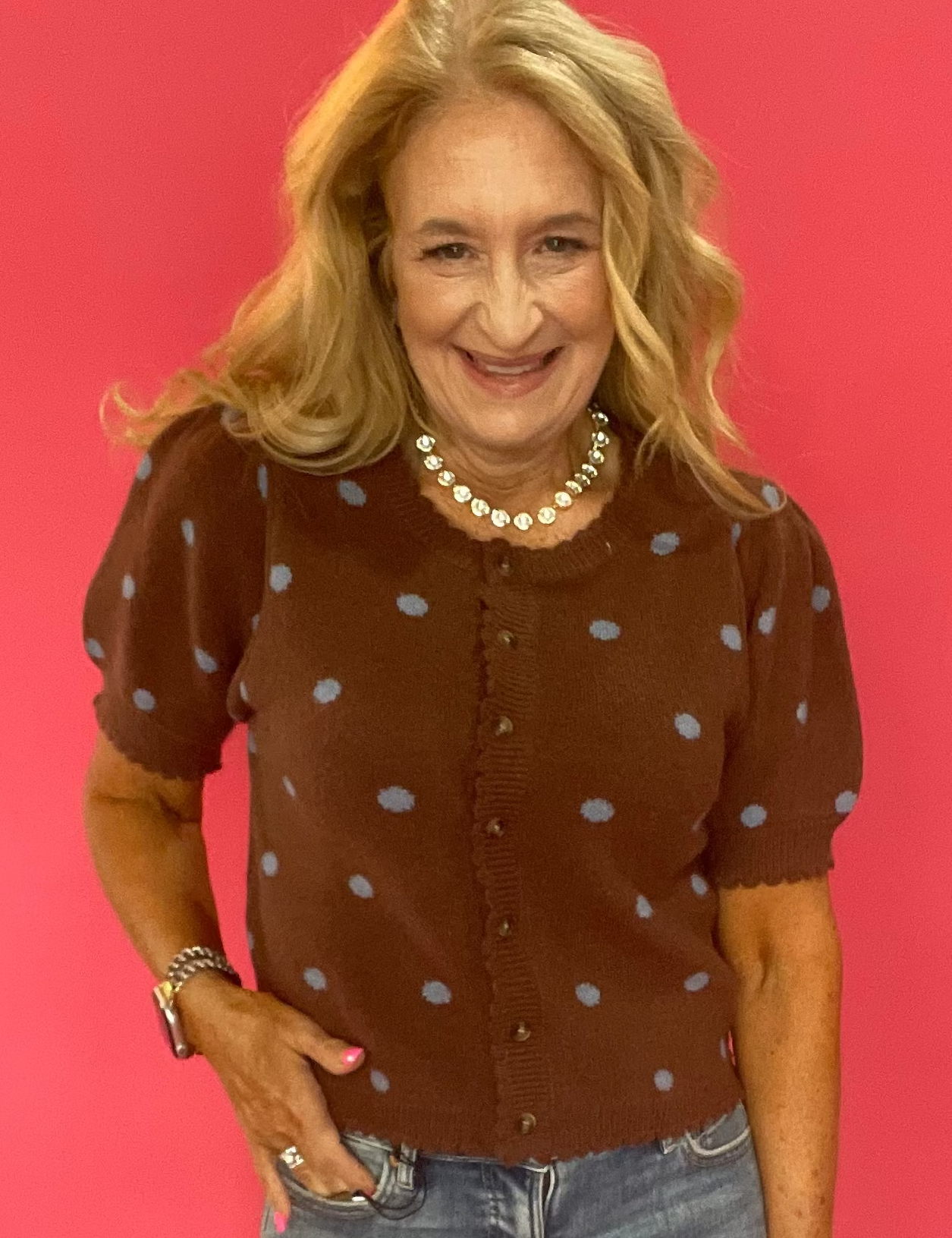 Woman wearing a cocoa brown polka dot cardigan styled open over a simple top with denim
