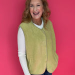 Woman wearing a bright chartreuse green sherpa vest buttoned over a plaid shirt and jeans