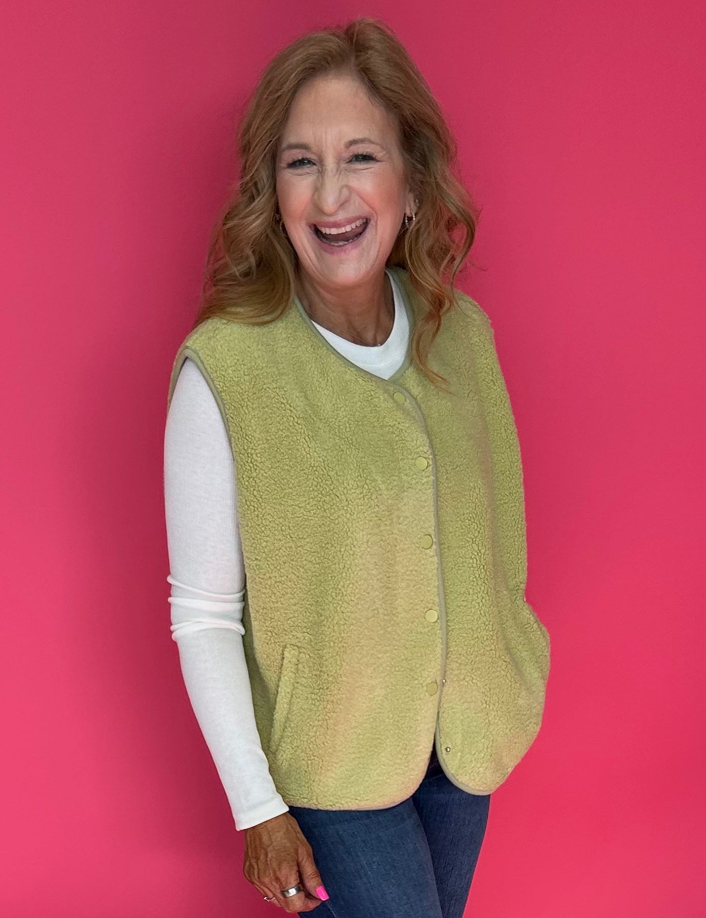 Woman wearing a bright chartreuse green sherpa vest buttoned over a plaid shirt and jeans