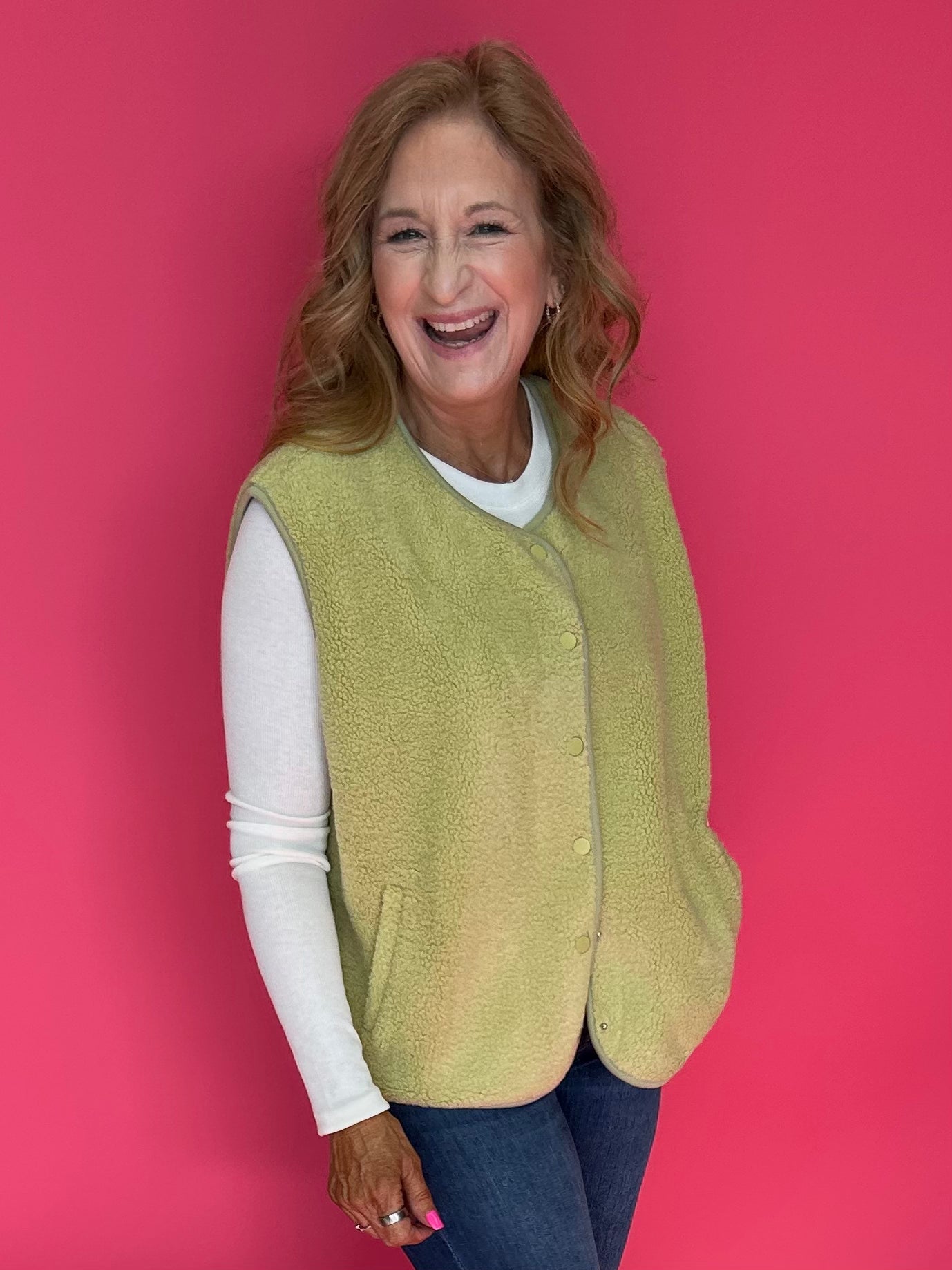 Woman wearing a bright chartreuse green sherpa vest buttoned over a plaid shirt and jeans