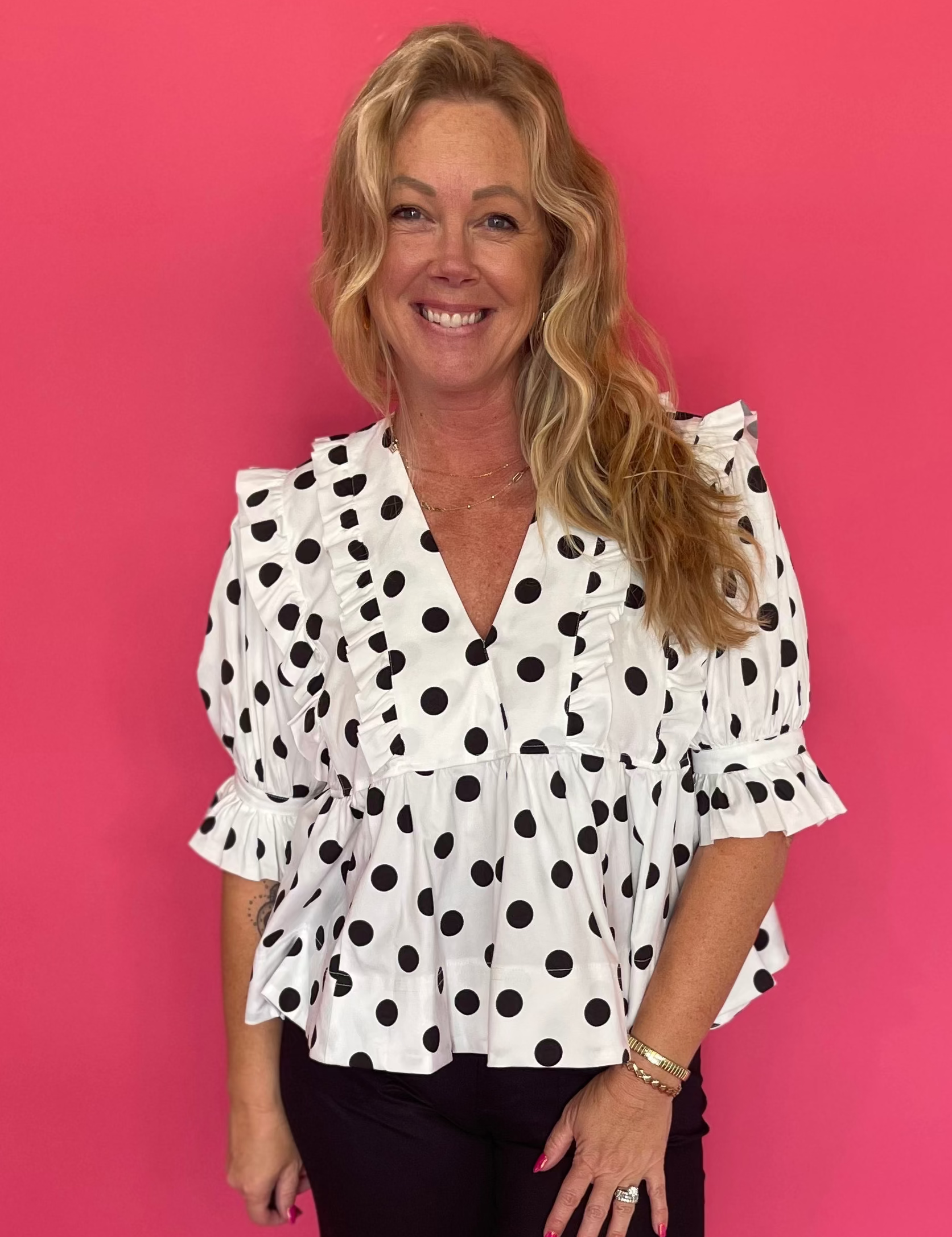Woman wearing a black and white polka dot babydoll top with a deep ruffled V-neck and denim shorts