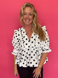 Woman wearing a black and white polka dot babydoll top with a deep ruffled V-neck and denim shorts