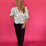 Close-up of the ruffle trim running down the deep V-neckline of the polka dot woven top