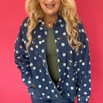 Woman wearing an oversized dark wash denim jacket with cream polka dots over a white tee and shorts