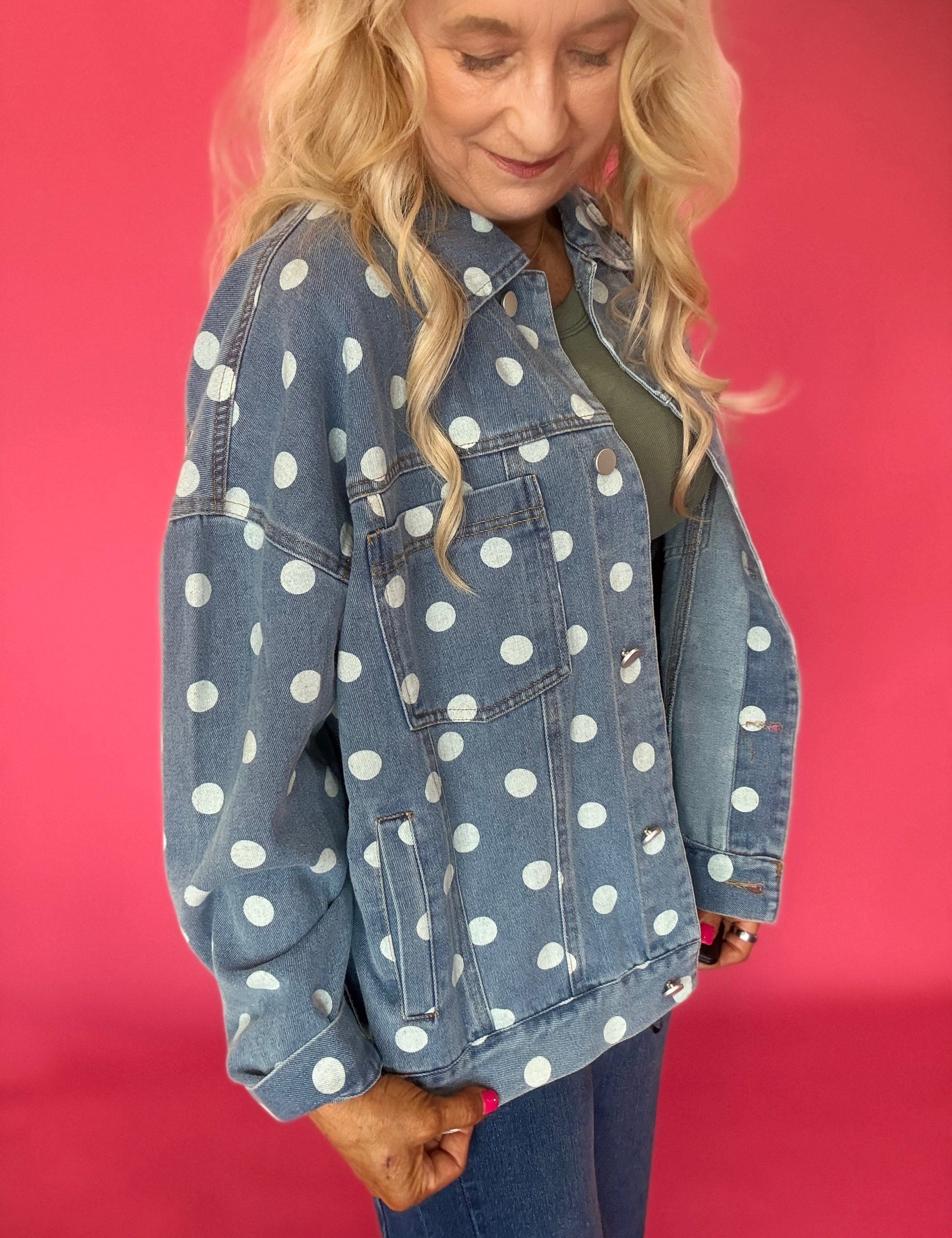Woman wearing an oversized light wash denim jacket covered in cream polka dots over a sundress