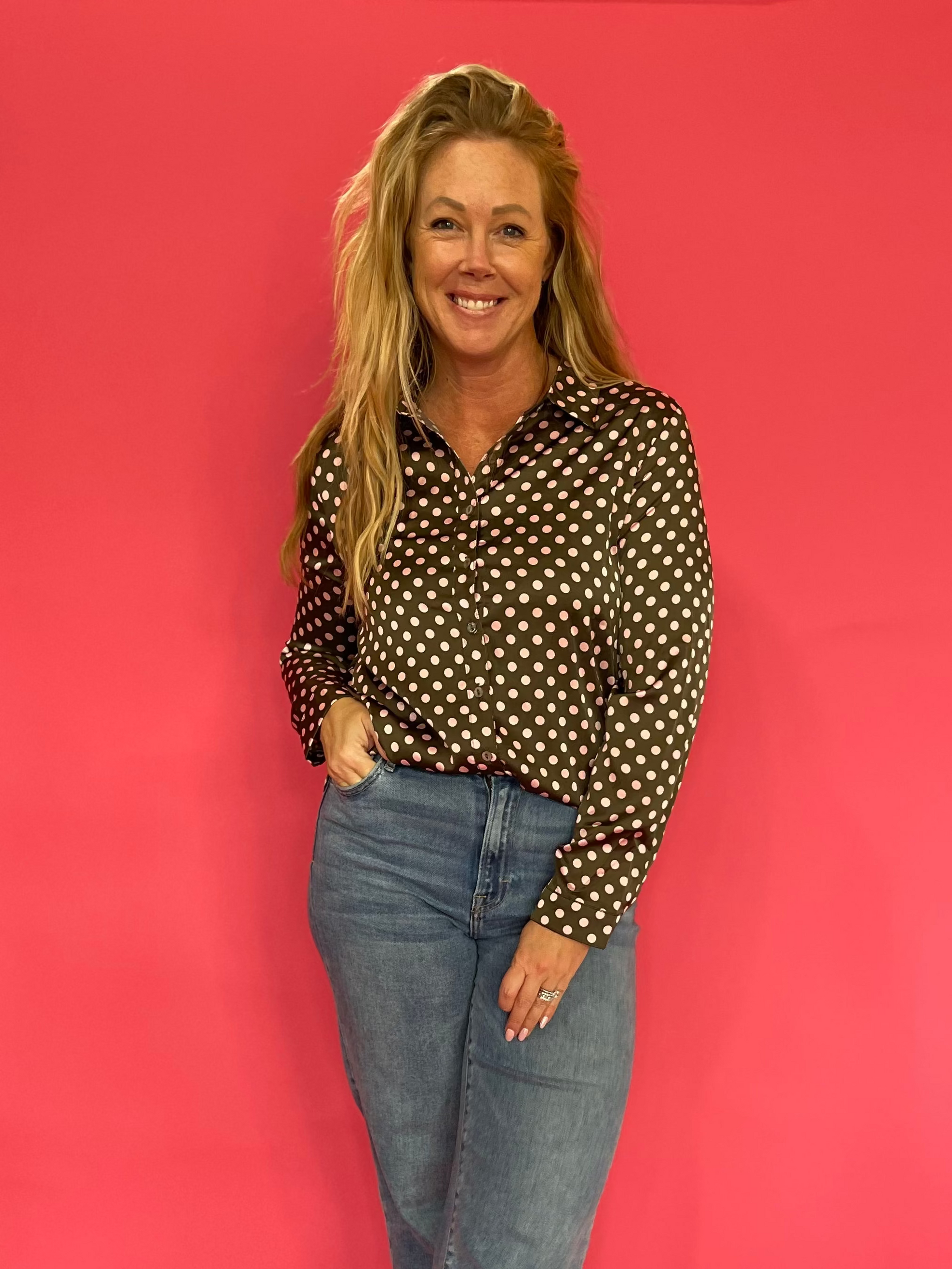 Woman wearing an olive polka dot satin button down shirt half tucked into high waist denim