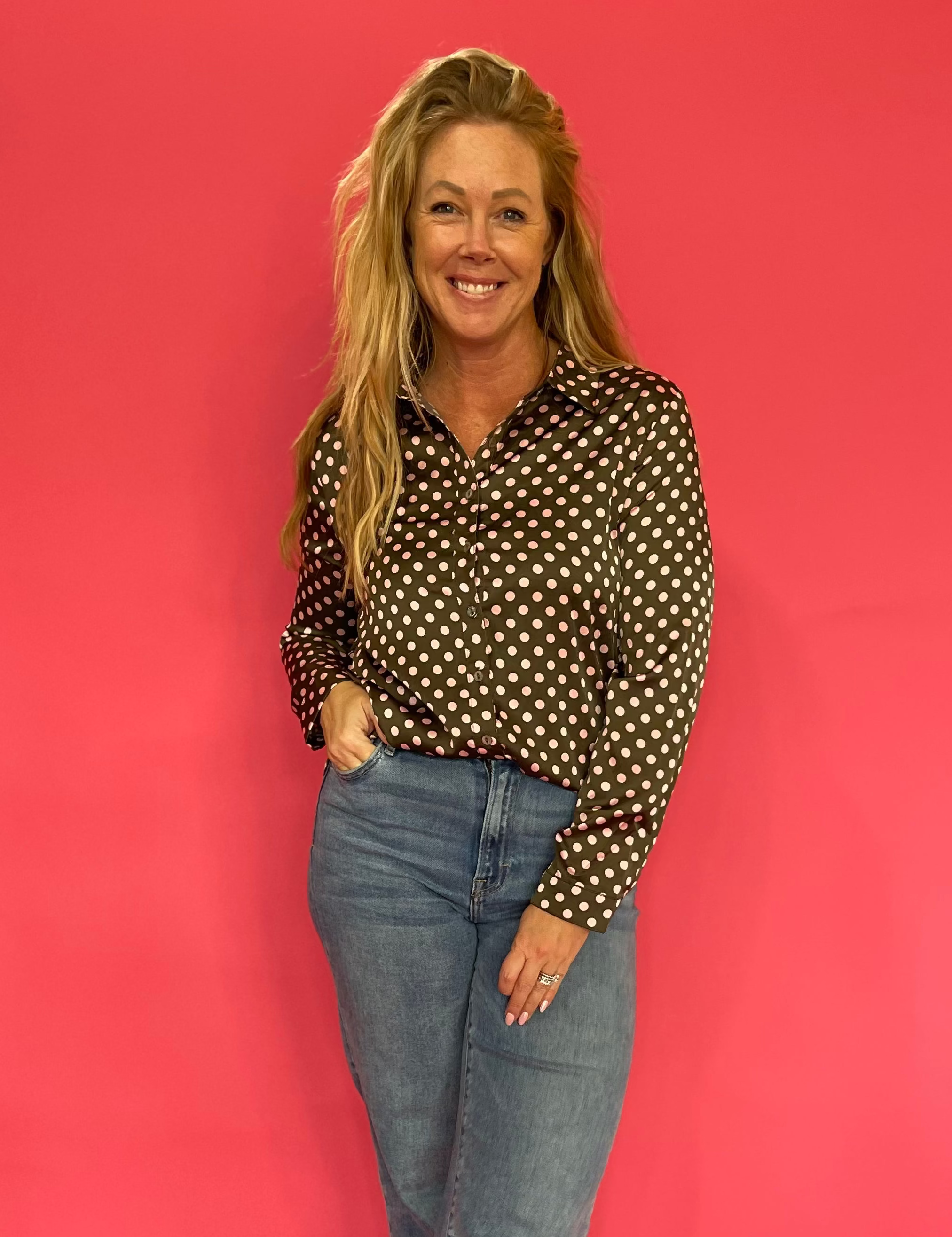 Woman wearing an olive polka dot satin button down shirt half tucked into high waist denim