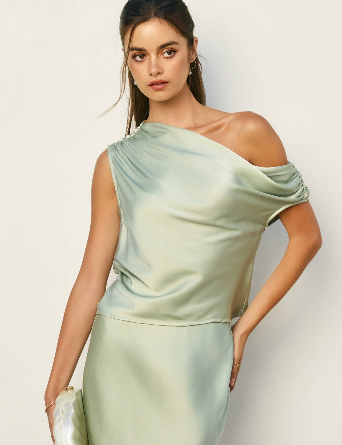 Woman wearing a light green one-shoulder dress against a plain background