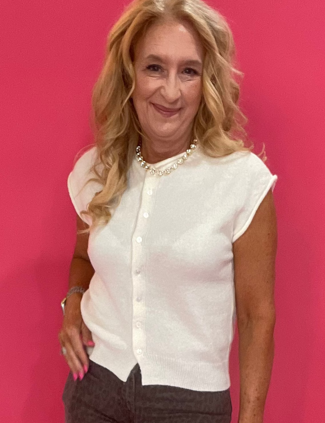 Woman wearing an ivory open-front sleeveless knit cardigan with raw edges over a fitted tee and jeans