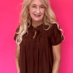 Woman wearing a lightweight brown woven blouse tucked into high waisted denim with an easy drape