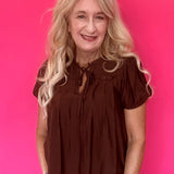 Woman wearing a lightweight brown woven blouse tucked into high waisted denim with an easy drape
