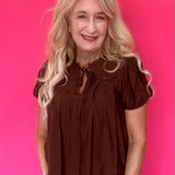 Woman wearing a lightweight brown woven blouse tucked into high waisted denim with an easy drape