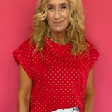 Woman wearing a red polka dot top and white shorts against a pink background