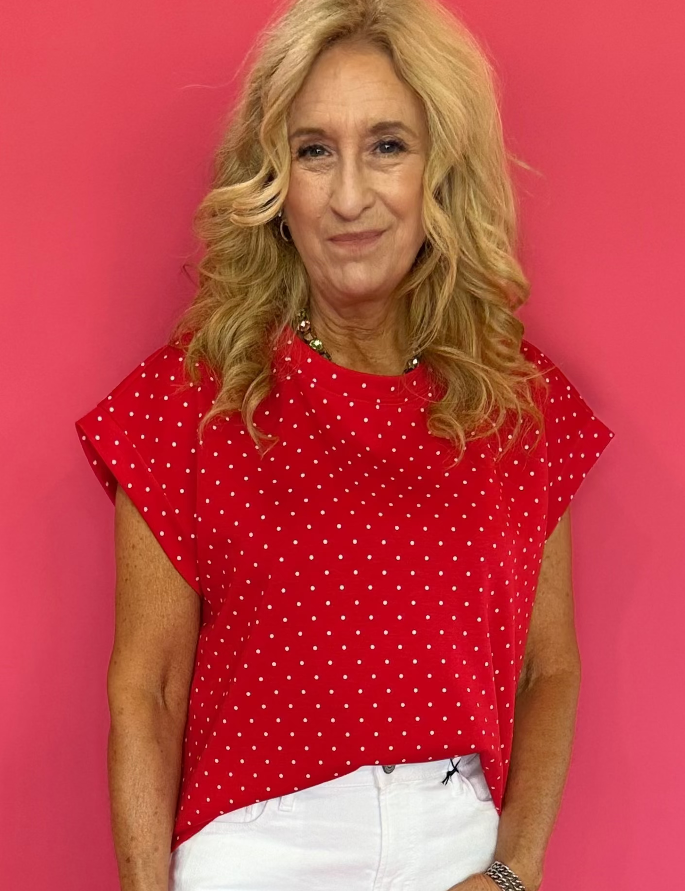 Woman wearing a red polka dot top and white shorts against a pink background