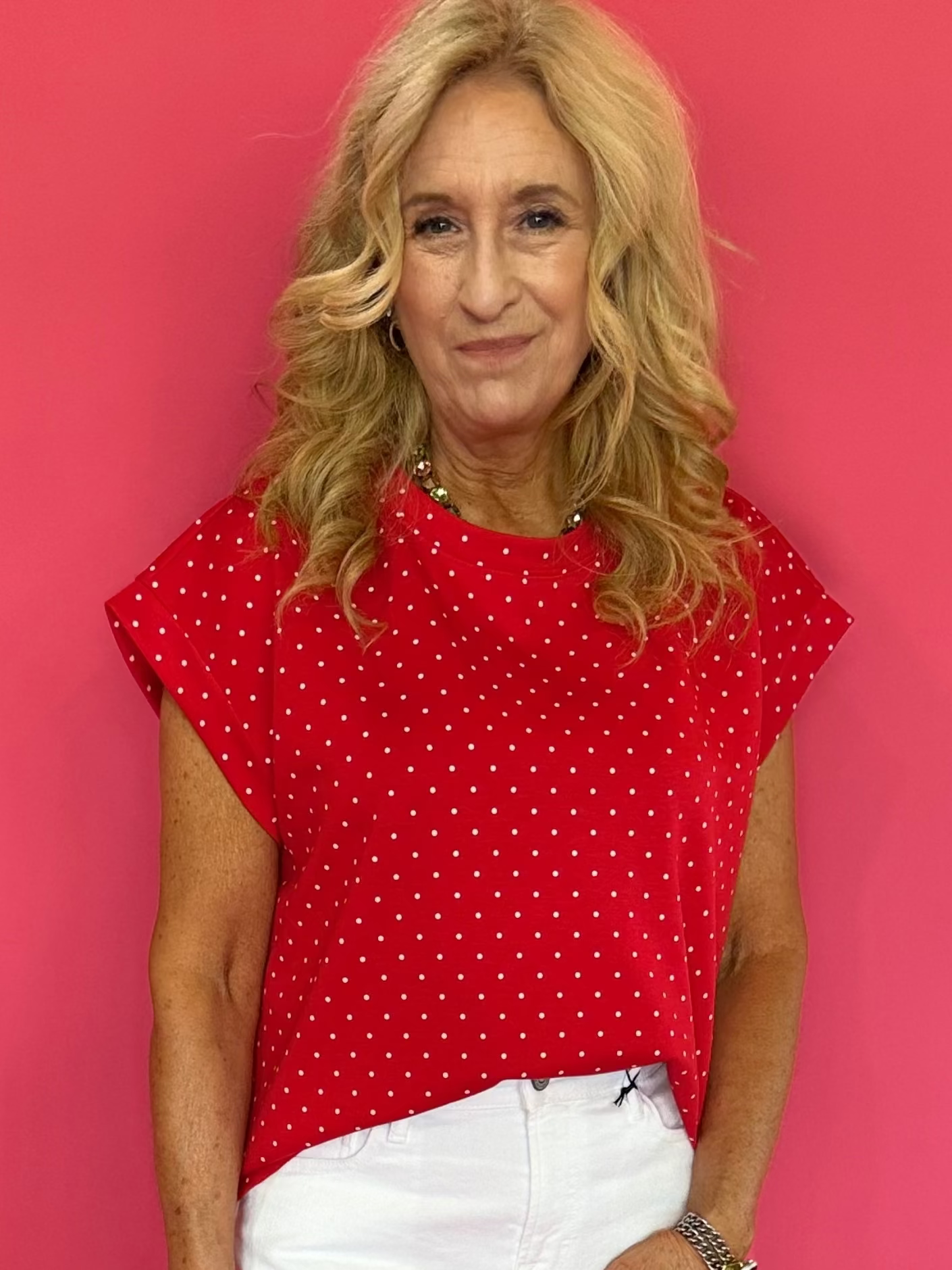 Woman wearing a red polka dot top and white shorts against a pink background