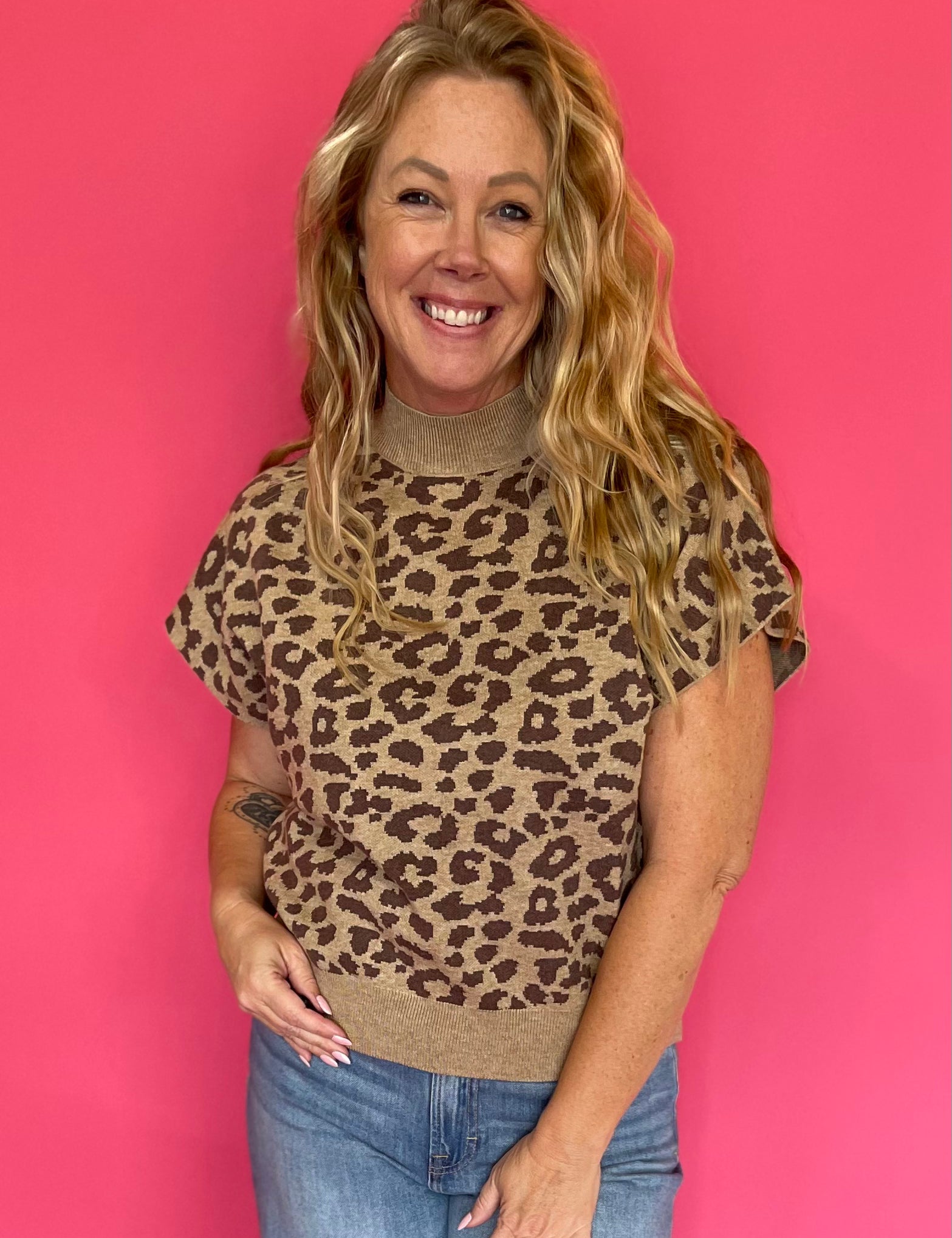 Woman wearing a leopard print knit top with a mock neckline and extended cap sleeves