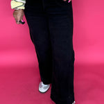 Woman wearing black high rise wide leg jeans with a wide roll up hem and a fitted turtleneck