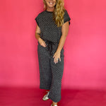 Woman wearing a charcoal micro polka dot scuba lounge set with a cap sleeve top and wide leg pants