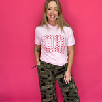 Person wearing a pink t-shirt with a red pattern and camouflage pants on a pink background