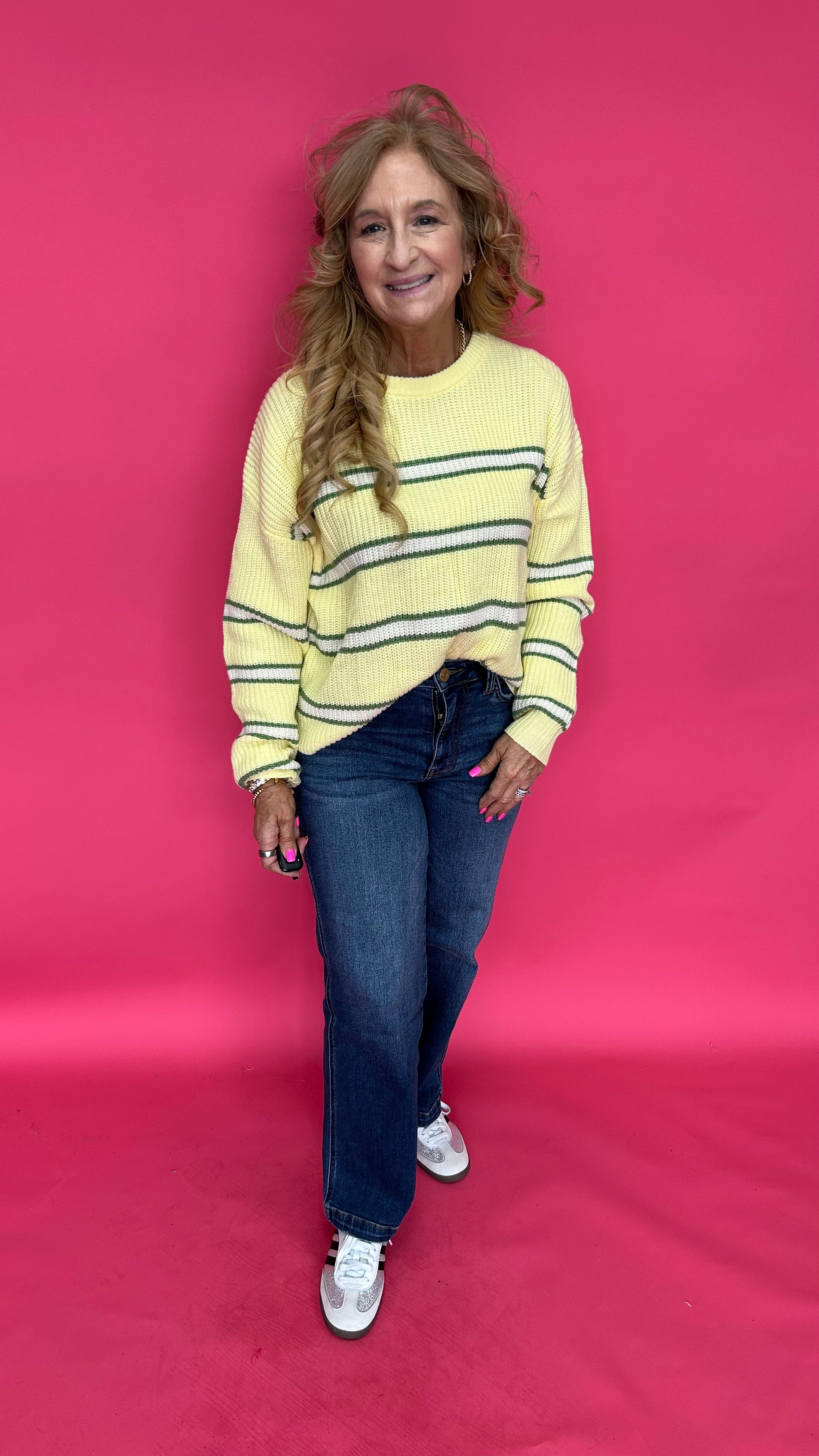 Woman wearing a yellow striped sweater and blue jeans on a pink background