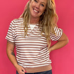 Woman wearing a rust and white striped puff sleeve top with a ribbed round neckline and denim