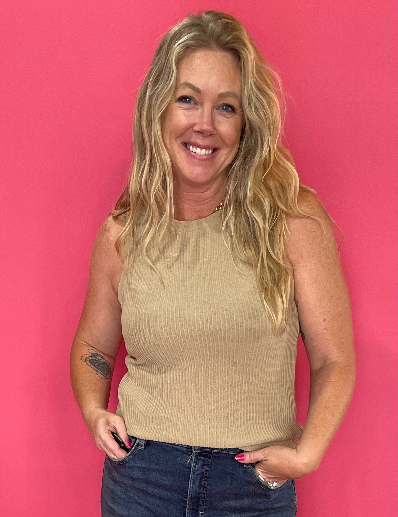 Woman wearing a mocha ribbed sweater knit tank tucked into high waisted denim with a belt