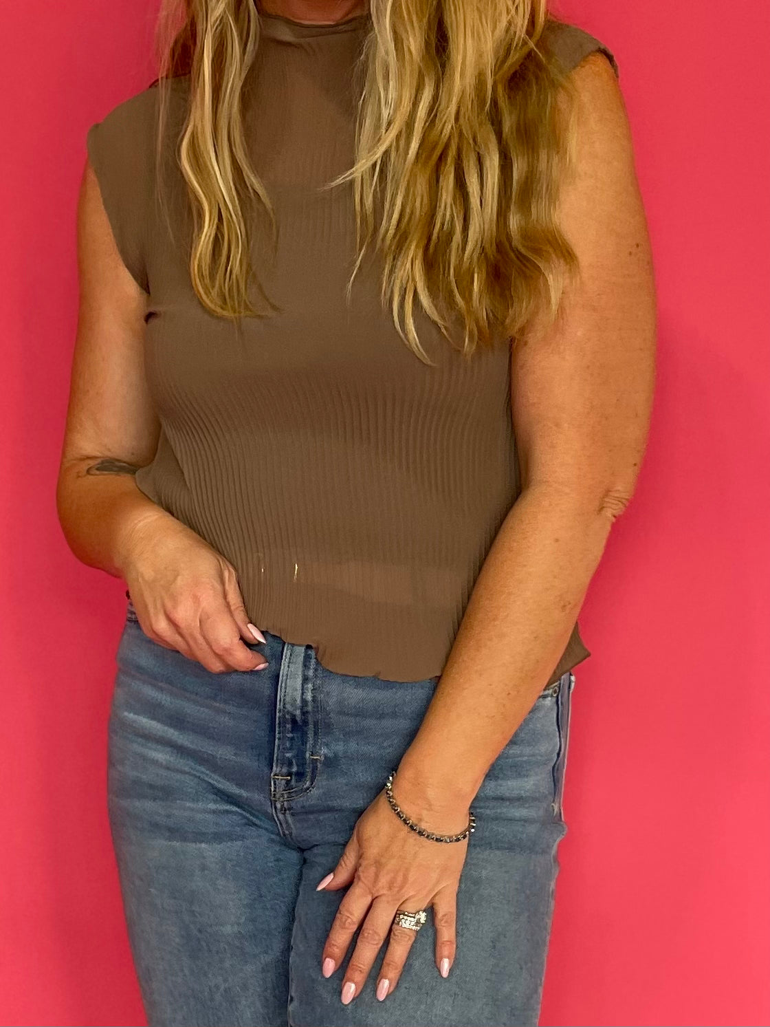 Woman wearing a mocha sheer plisse mock neck sleeveless blouse layered over a cami