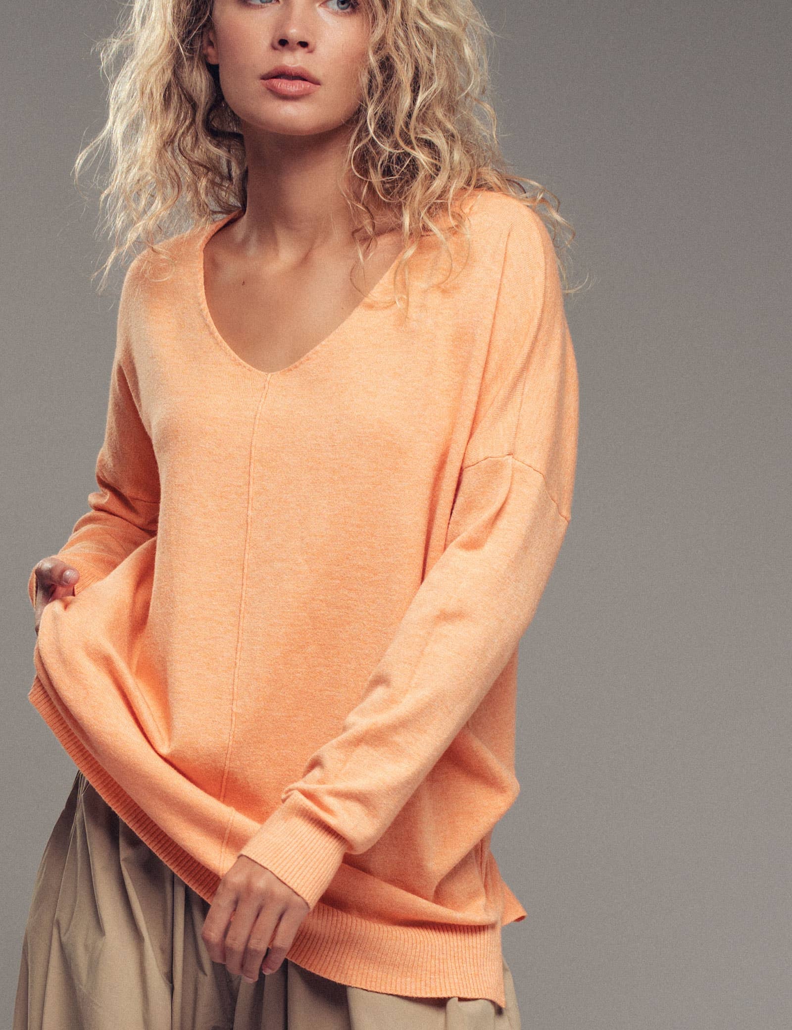 Woman wearing an orange sweater against a gray background