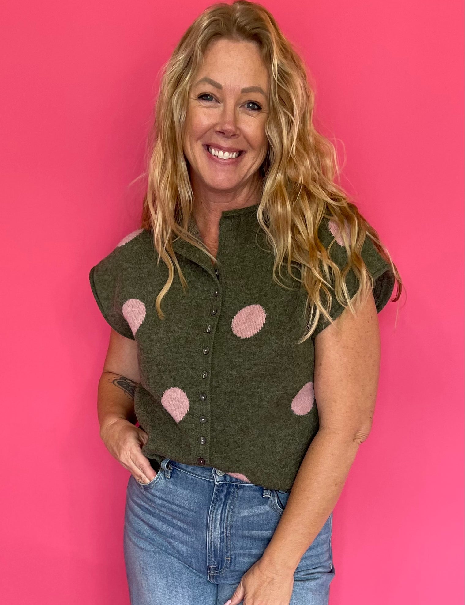 Woman wearing an olive green knit sweater top with blush polka dots, a collar and button front