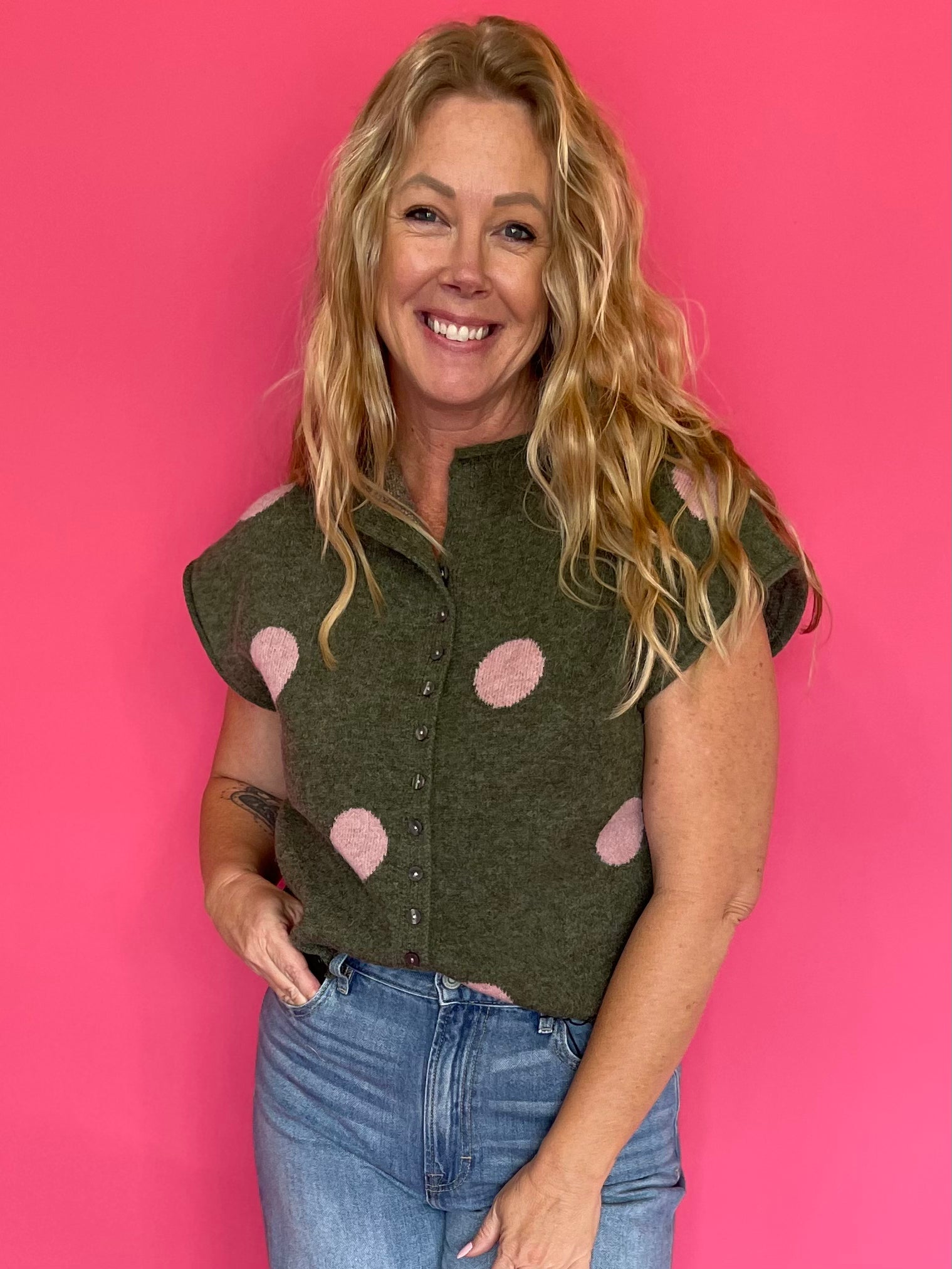 Woman wearing an olive green knit sweater top with blush polka dots, a collar and button front
