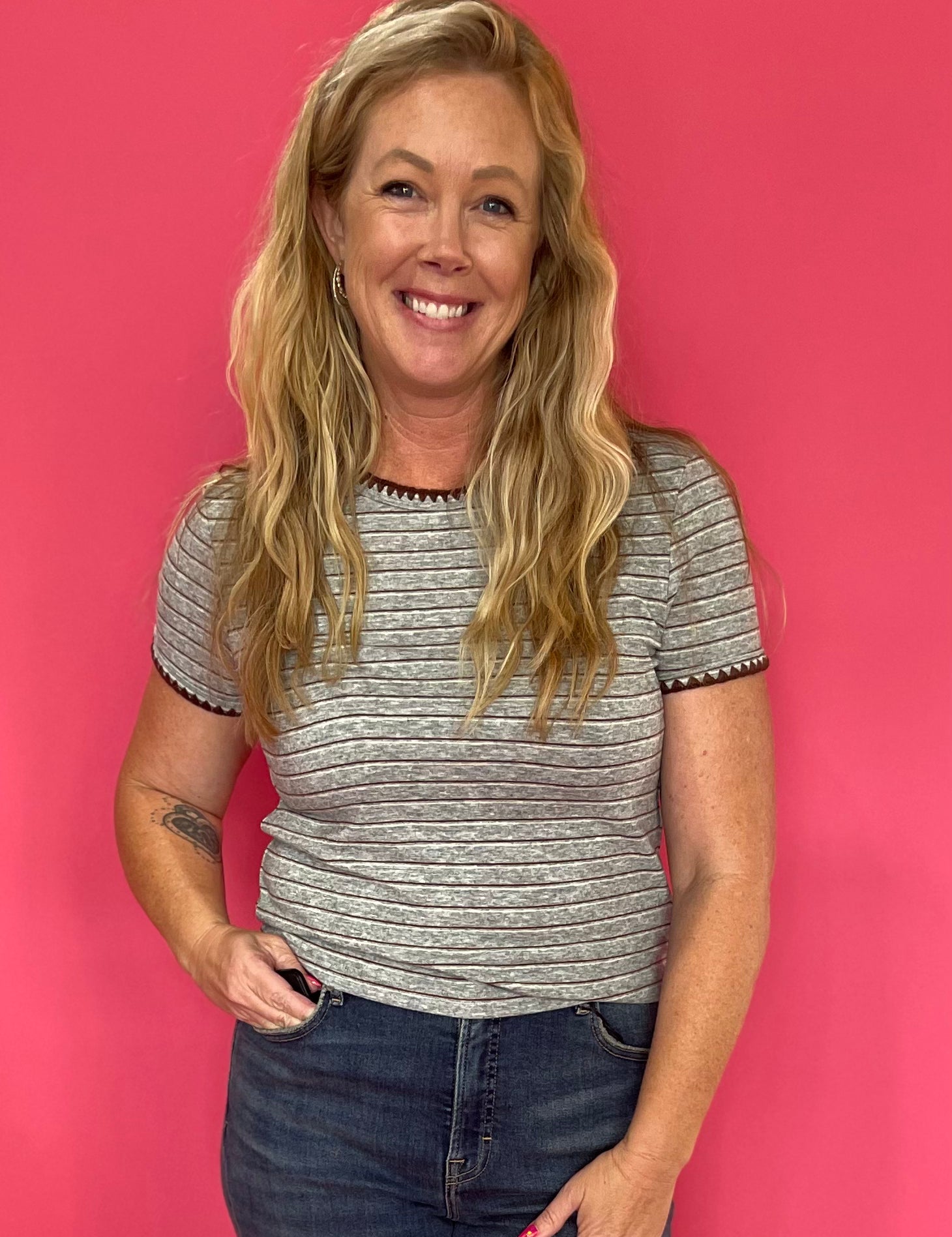 Woman wearing a fitted grey striped baby tee with a round neckline and short sleeves with high-rise jeans