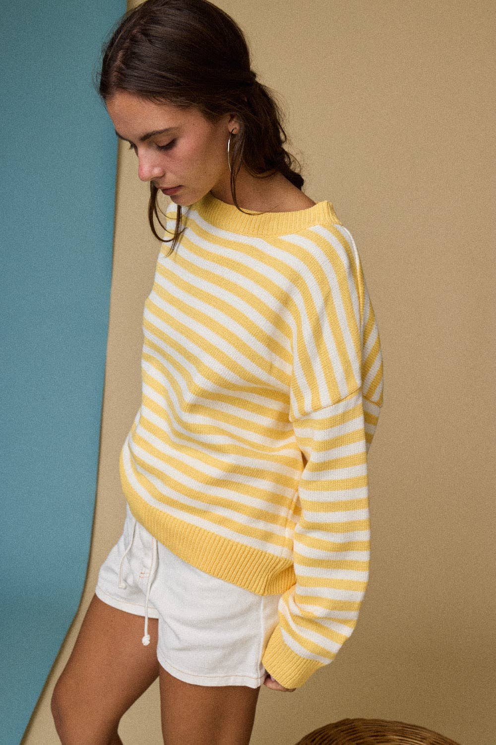 Woman wearing a yellow and white striped sweater against a beige wall.