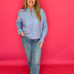 Woman wearing a blue shirt with pink polka dots and jeans against a red background