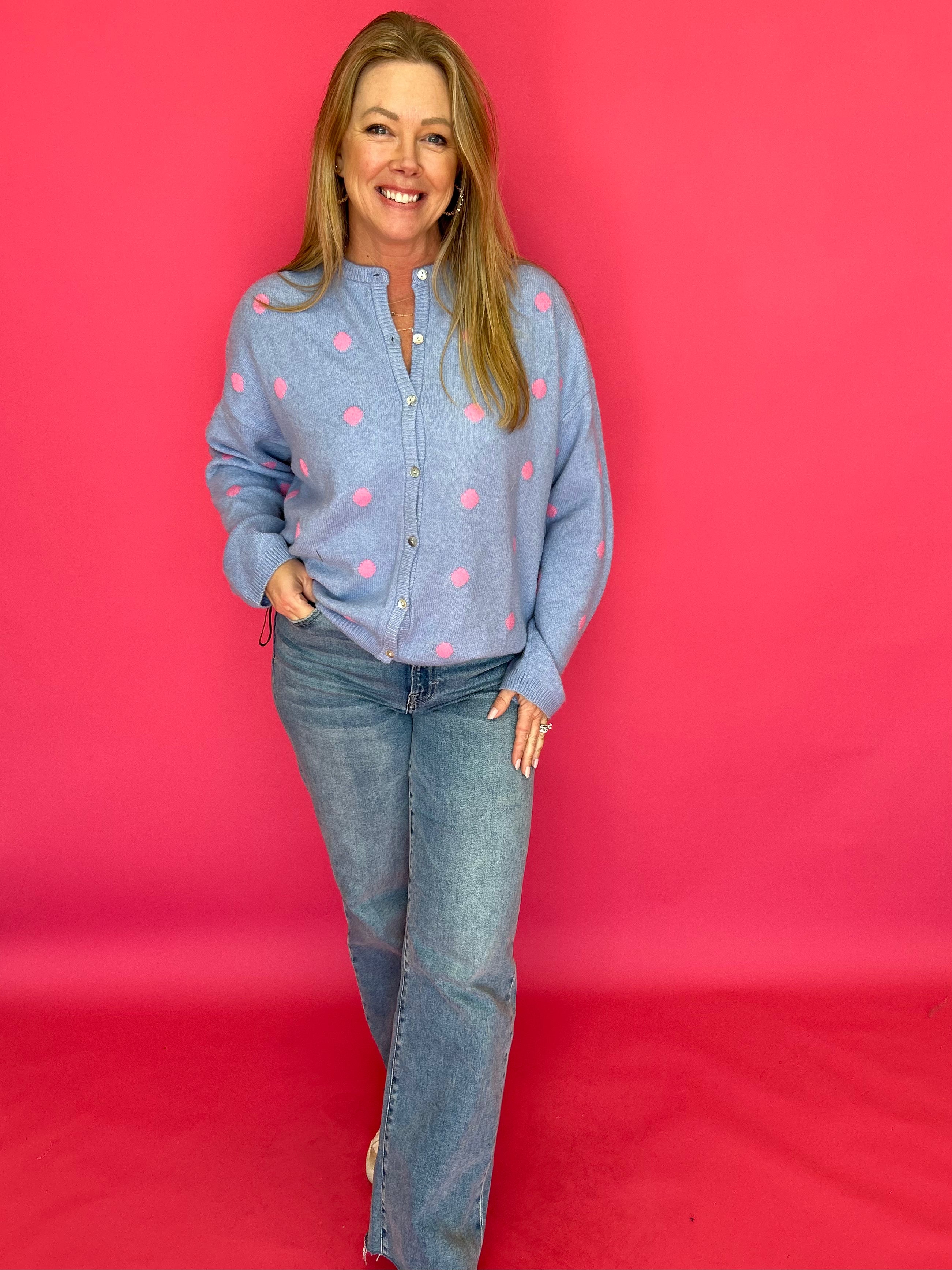 Woman wearing a blue shirt with pink polka dots and jeans against a red background