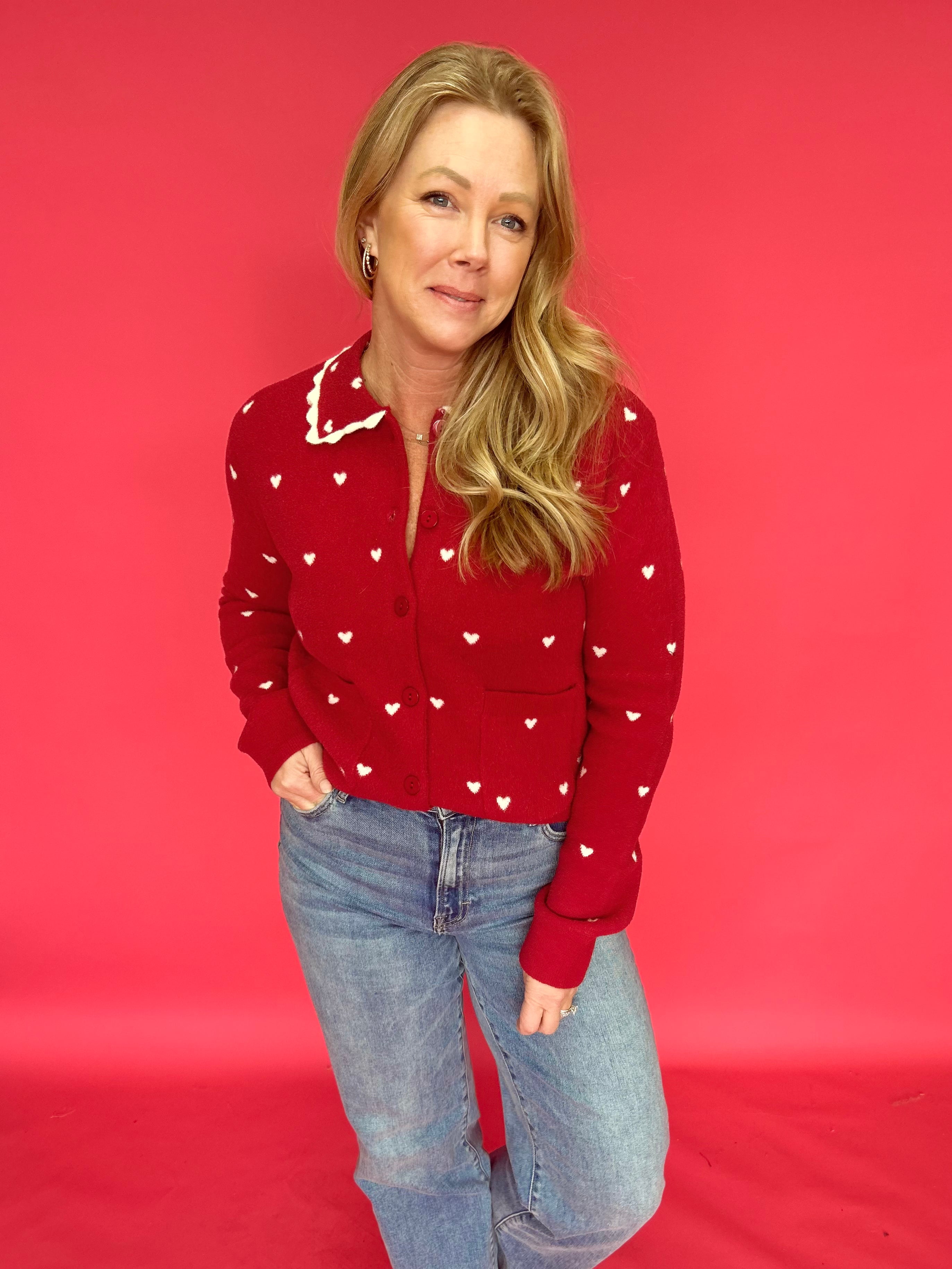 Woman wearing a red all-over heart print button-up sweater with a scalloped heart collar