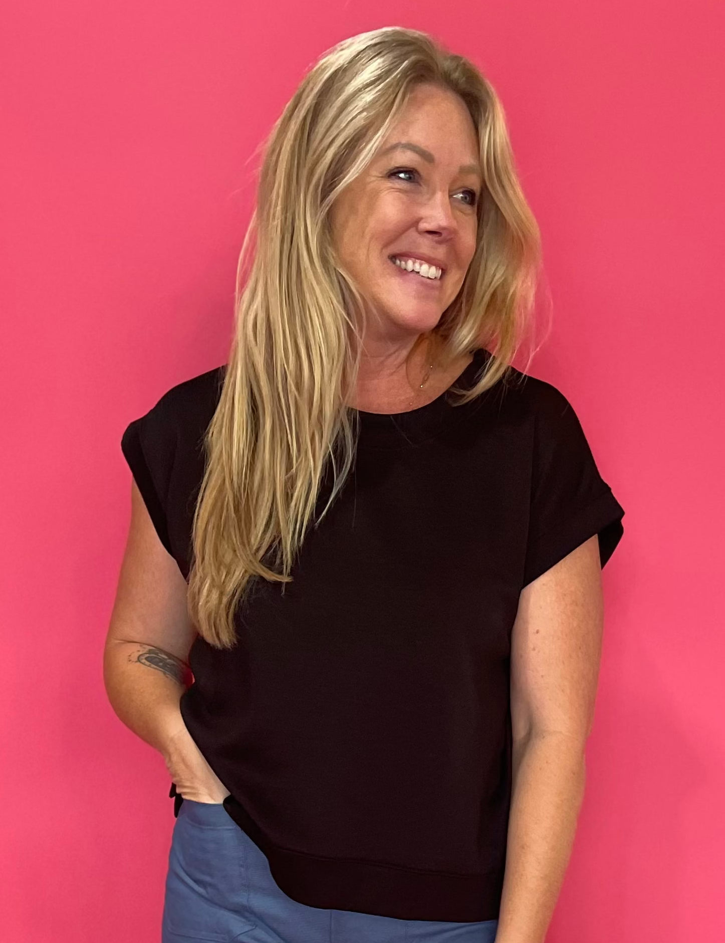 Woman wearing a black scuba knit short sleeve top with a relaxed fit, front tucked into denim