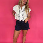 Close-up of the navy scallop ruffle trim and button front on the white woven top
