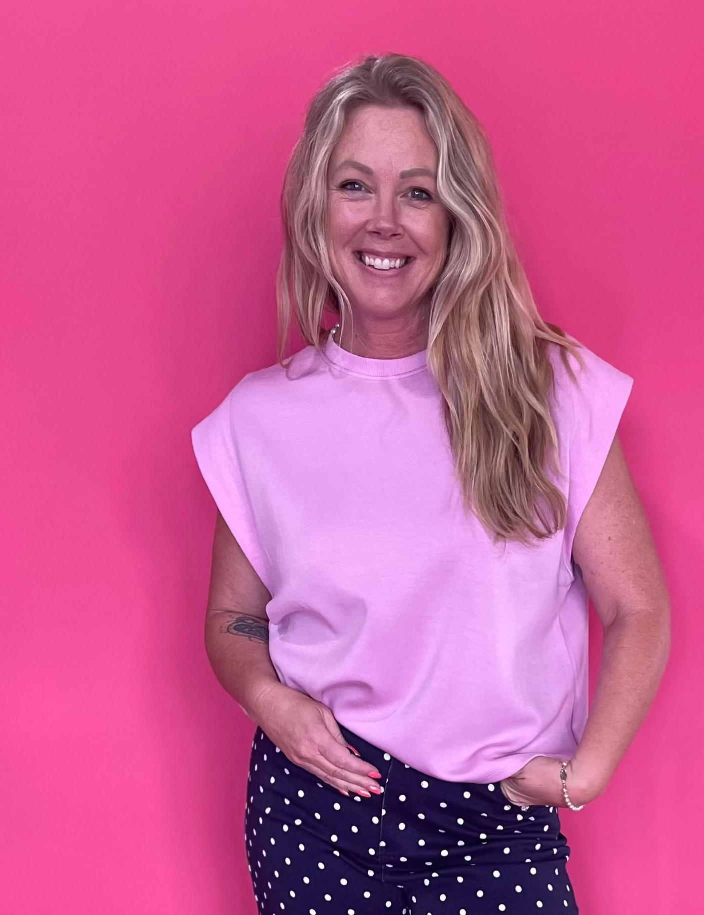 Woman wearing a light pink sleeveless top with structured shoulders and wide leg jeans