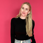 Person wearing a black top and light-colored pants against a pink background