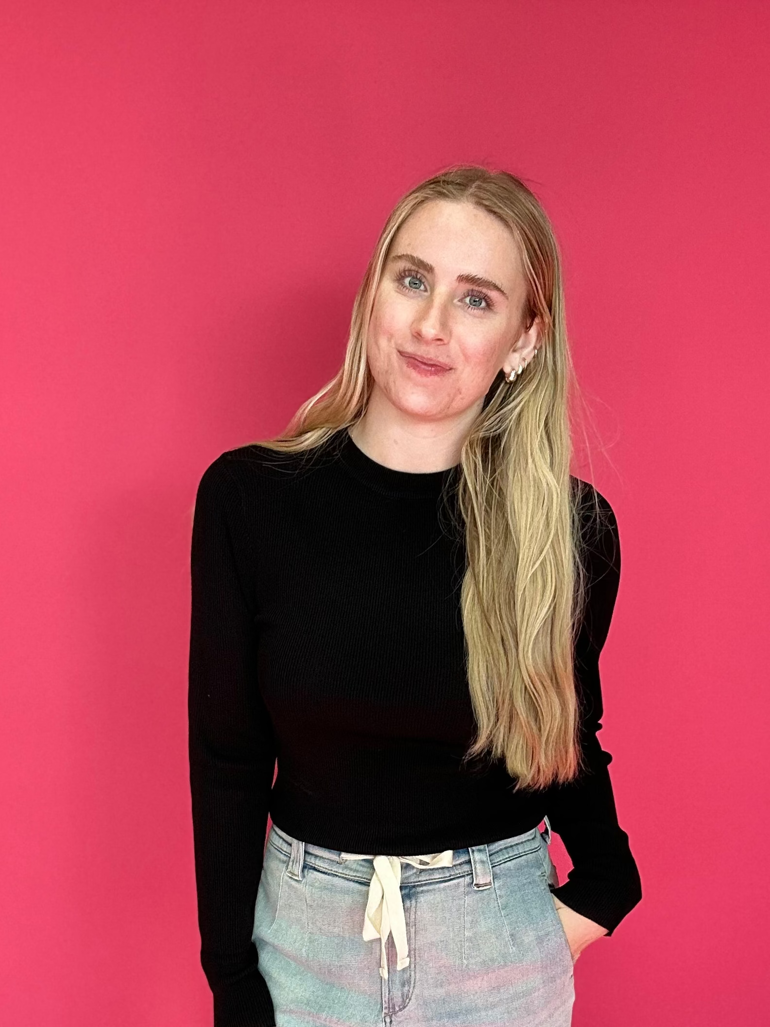 Person wearing a black top and light-colored pants against a pink background