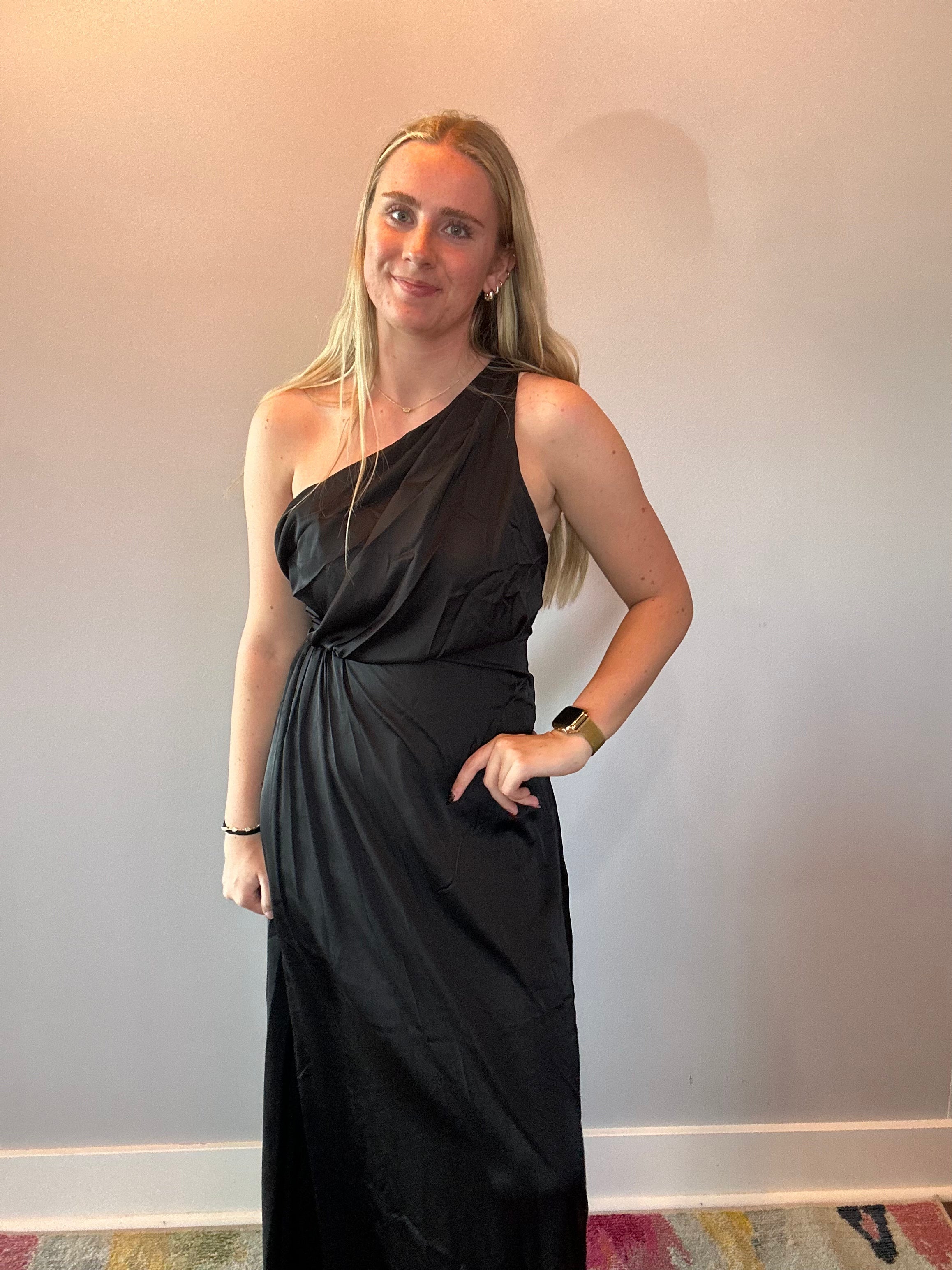 Full length view of the black one-shoulder dress styled with heels for an evening event