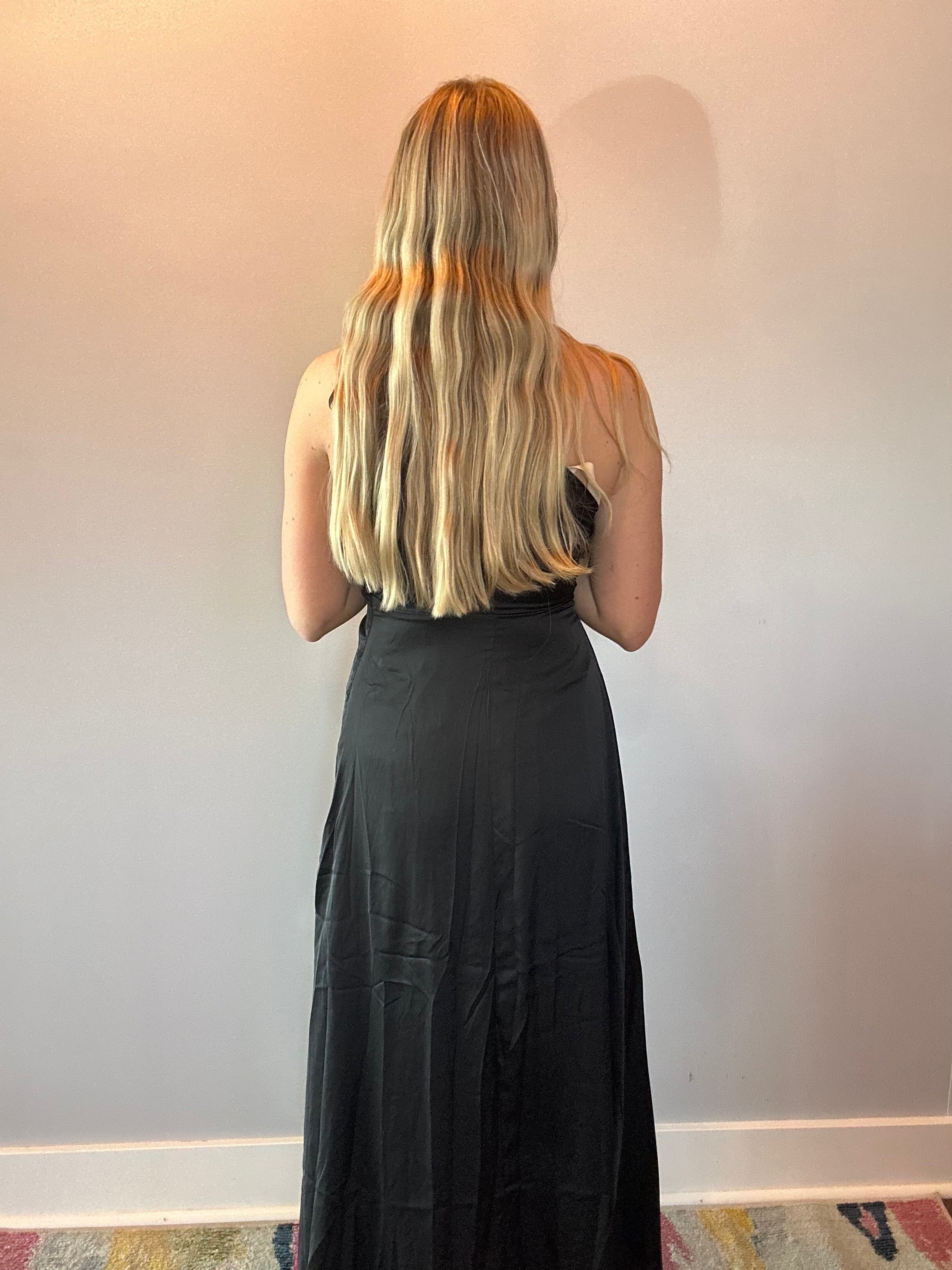 Black draped one-shoulder dress styled for a wedding reception with simple jewelry and a clutch