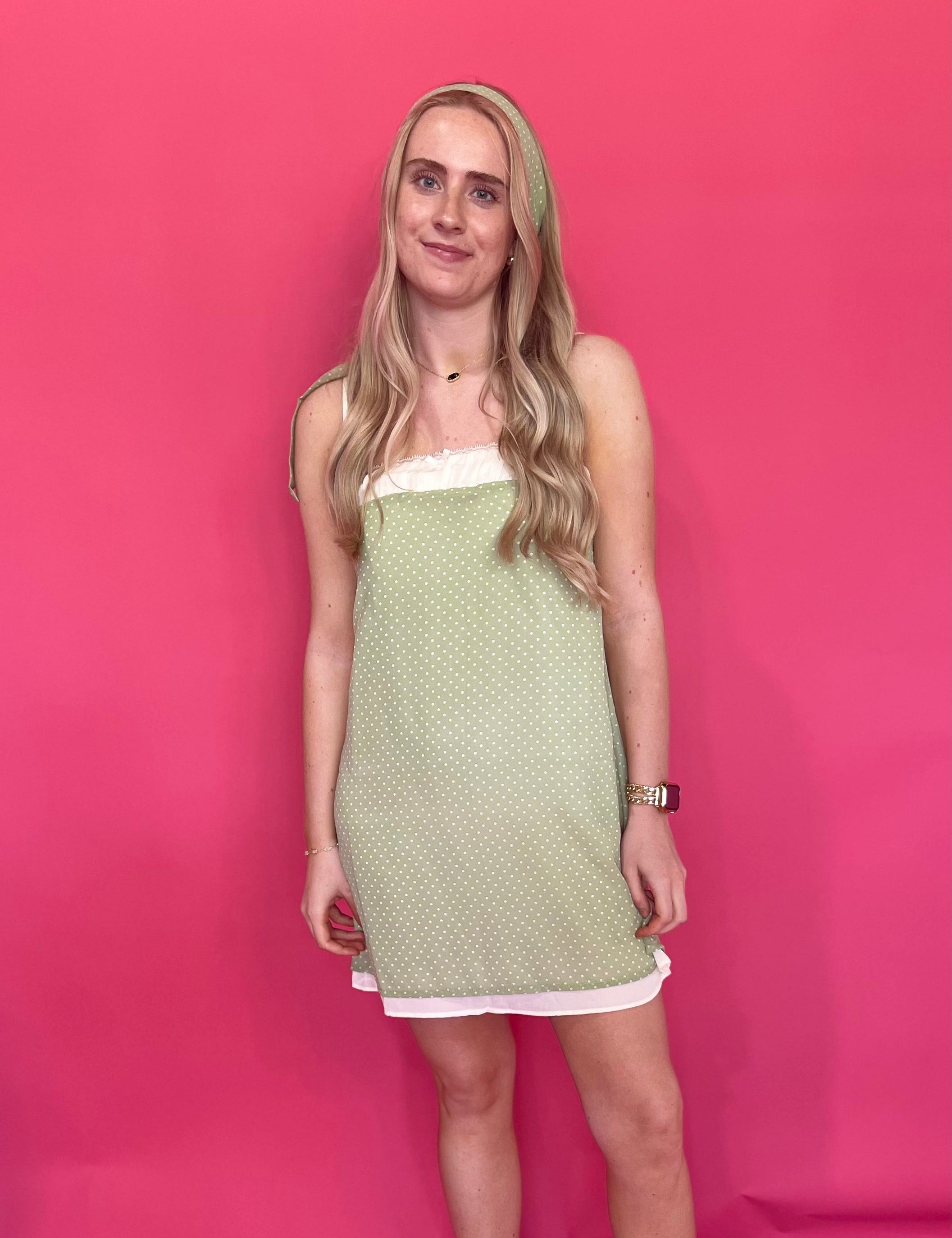 Woman wearing a sage green polka dot mini dress with lace trim and adjustable spaghetti straps