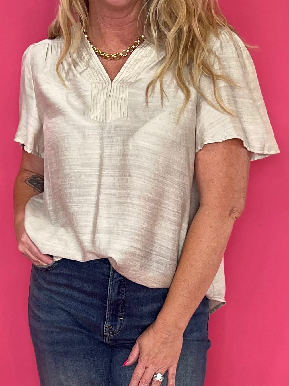 Woman wearing a soft oatmeal V-neck blouse with trapunto stitching and a relaxed flowy drape